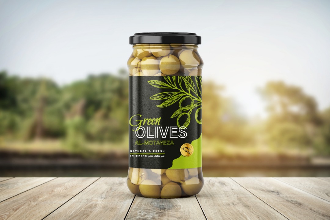 A jar of green olives on a wooden table with a blurred natural background